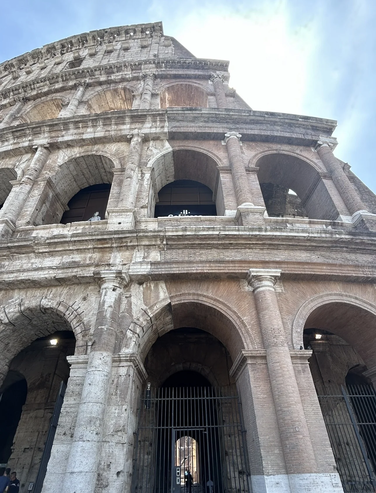 The outer arches of the Colosseum in Rome seen from below against a bright sky