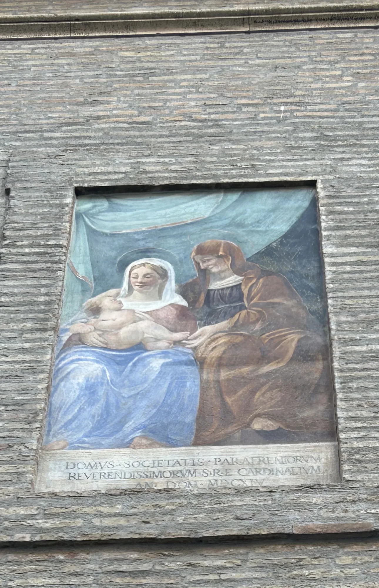 A street fresco of the Madonna and Child with St. Anne set into a brick wall in Rome, dated 1614