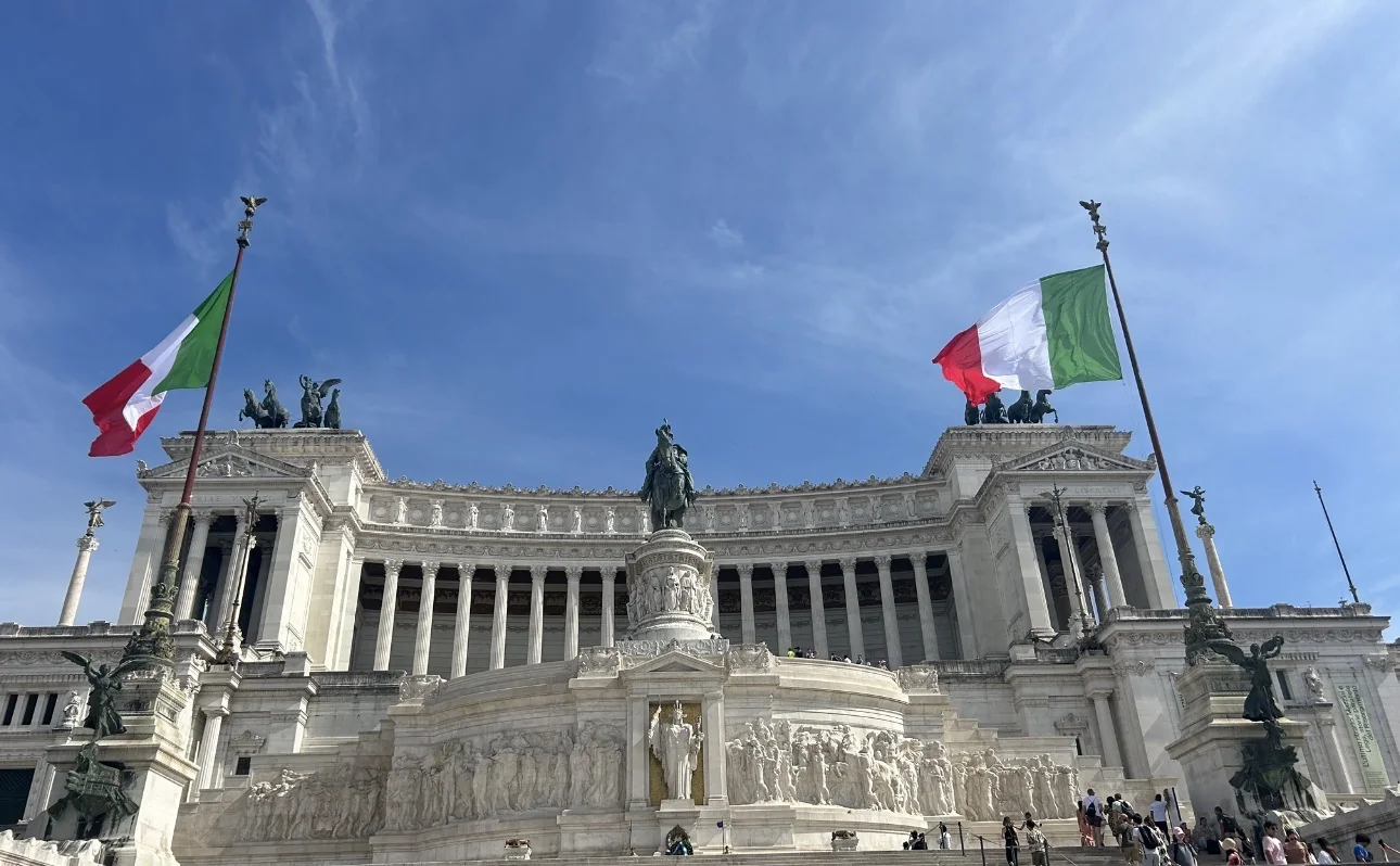 The Victor Emmanuel II Monument in Rome under a blue sky with two Italian flags