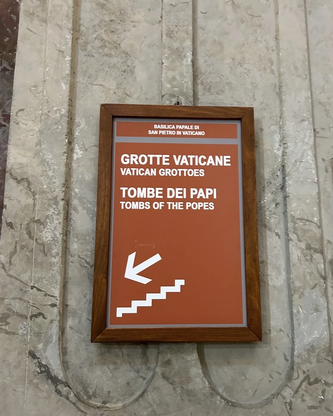 A sign in St. Peter's Basilica pointing down the stairs to the Vatican Grottoes and the Tombs of the Popes