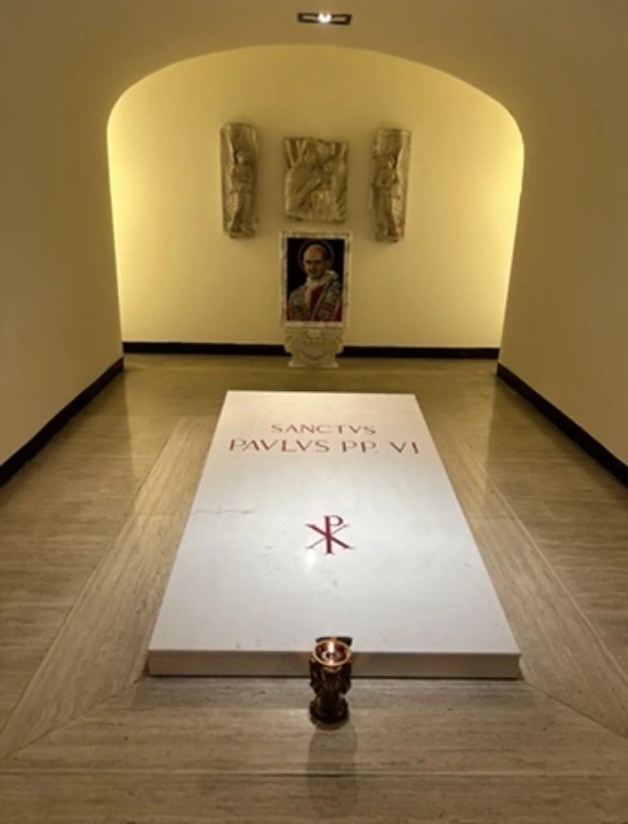 The tomb of St. Paul VI in the Vatican Grottoes beneath St. Peter's Basilica, a plain marble slab with a lit lamp
